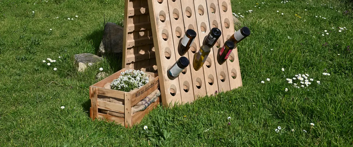 Rüttelpulte Im Anschnitt ist ein großes Rüttelpult für 120 Flaschen im Garten zu sehen. Nebendran steht dekorativ eine bepflanzte Kiste.