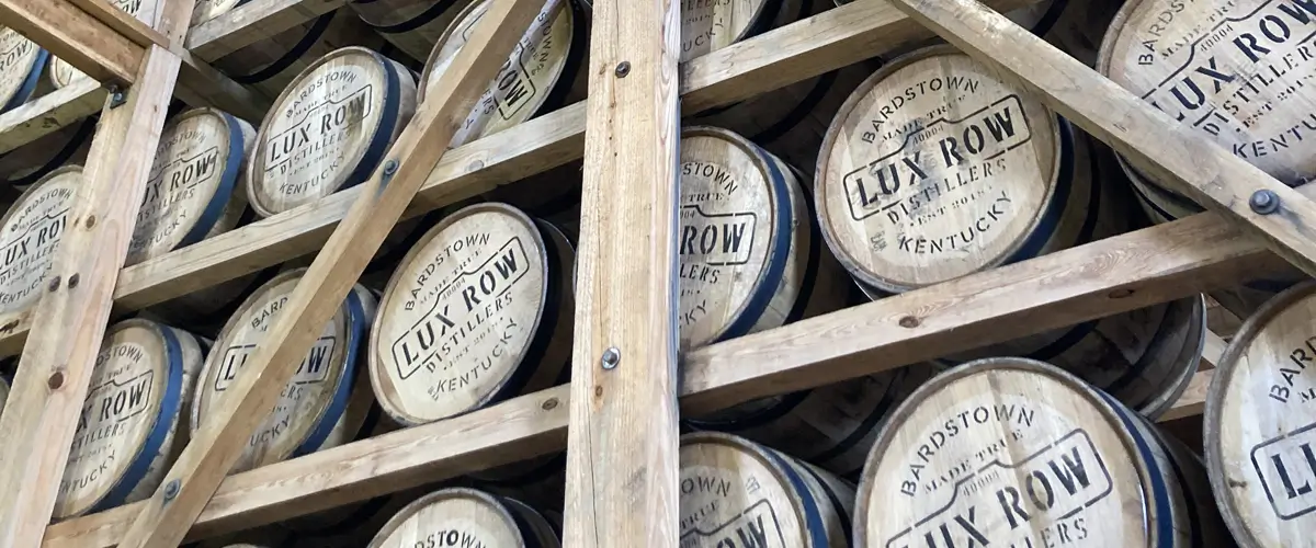 Man sieht viele liegende Fässer in einem Lager auf Balken liegen mit einem Logo auf dem Deckel „Lux Row“.